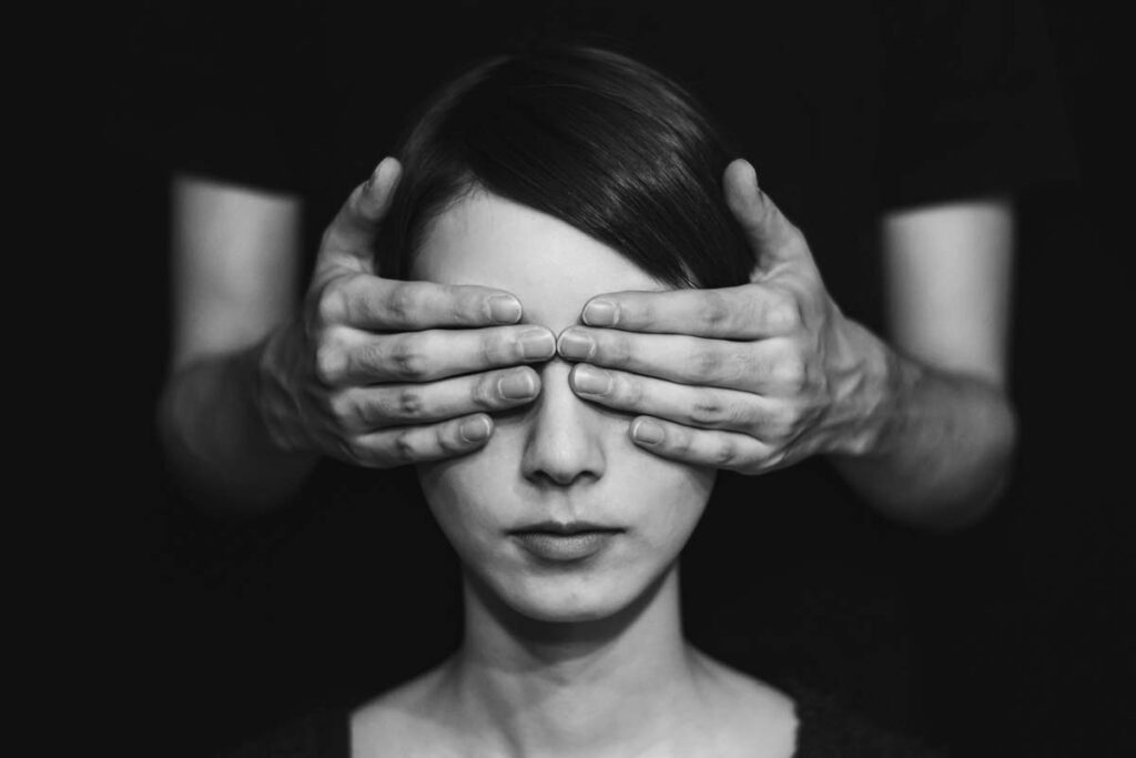 Frau, deren Augen von einer zweiten Person mit den Händen verdeckt werden